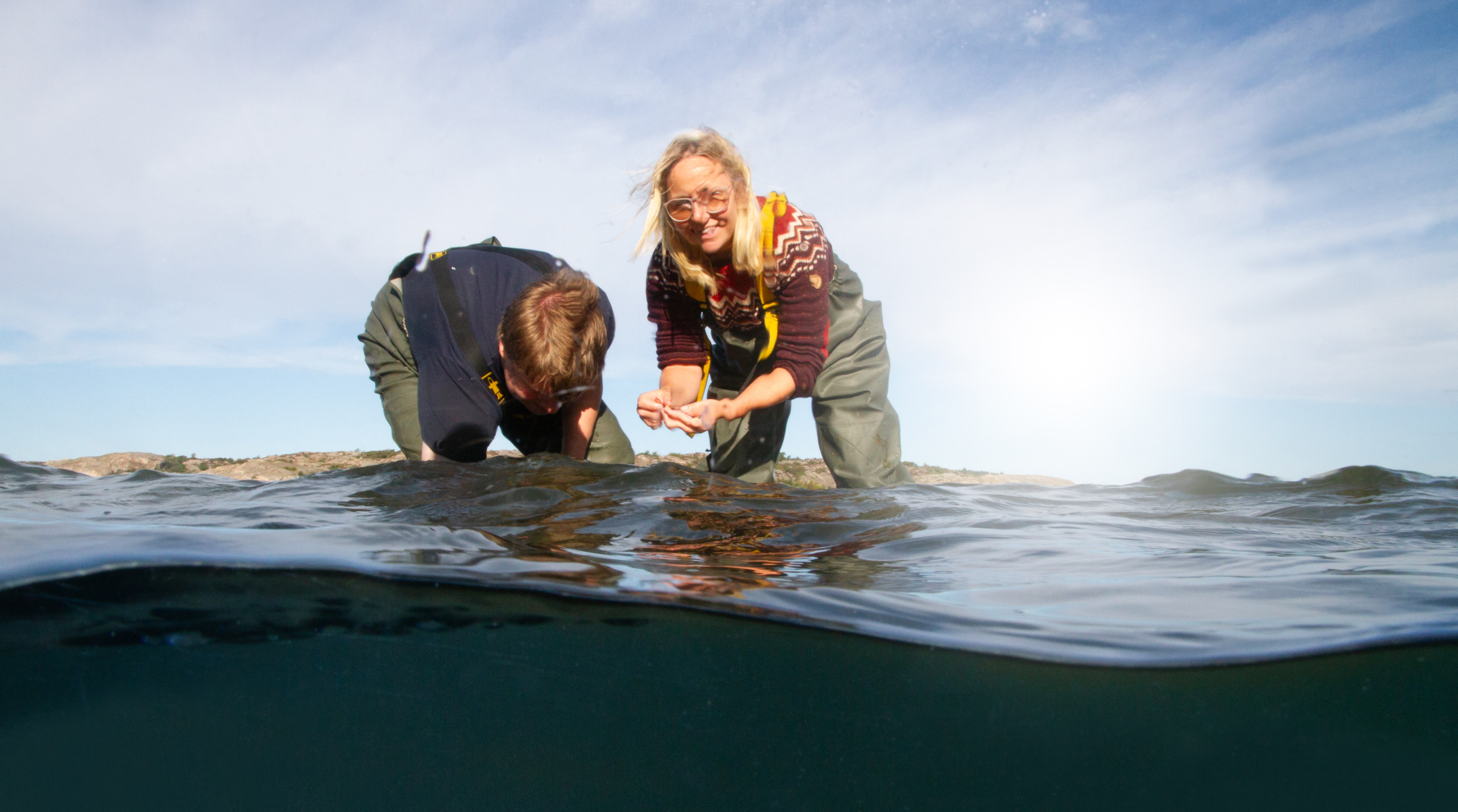 Två personer plockar upp saker från havsbotten.